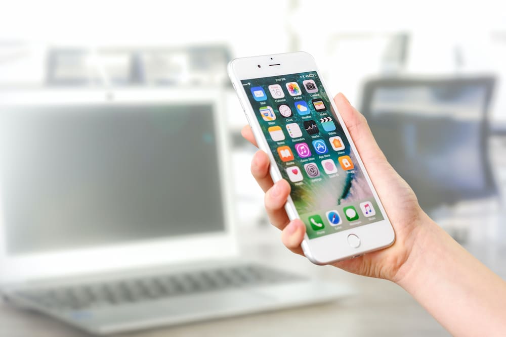 Mão segurando celular exibindo tela com diversos aplicativos.