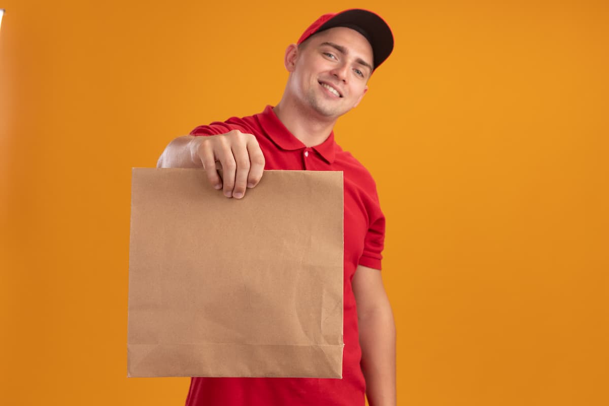 Entregador sorridente segurando um pacote de comida pedido pelos aplicativos de delivery.