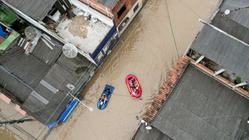 Vista de cima de moradores da Bahia usando botes para deixar suas residências em ruas alagadas.