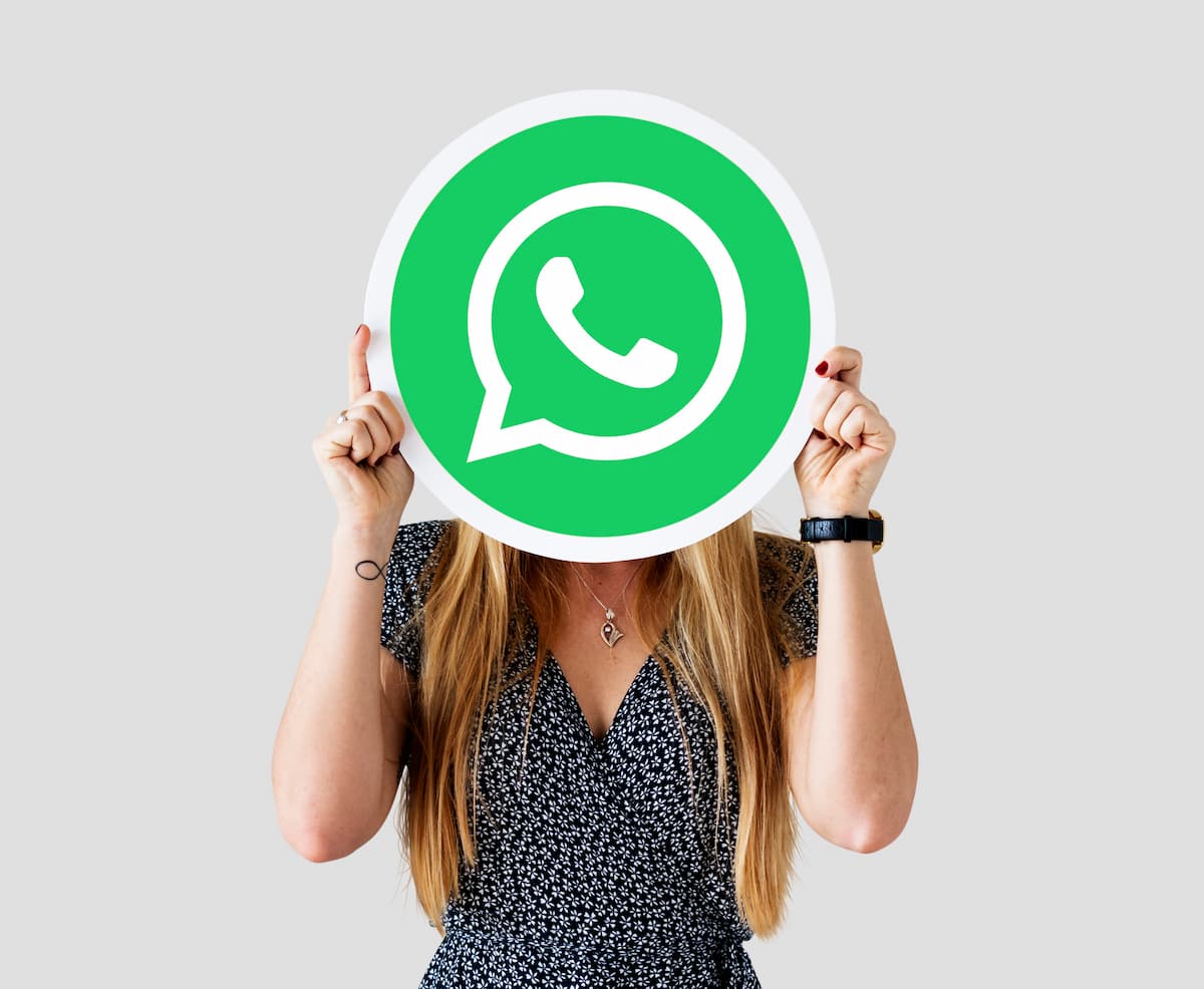 Mulher segurando placa com a logo do WhatsApp em frente ao seu rosto.