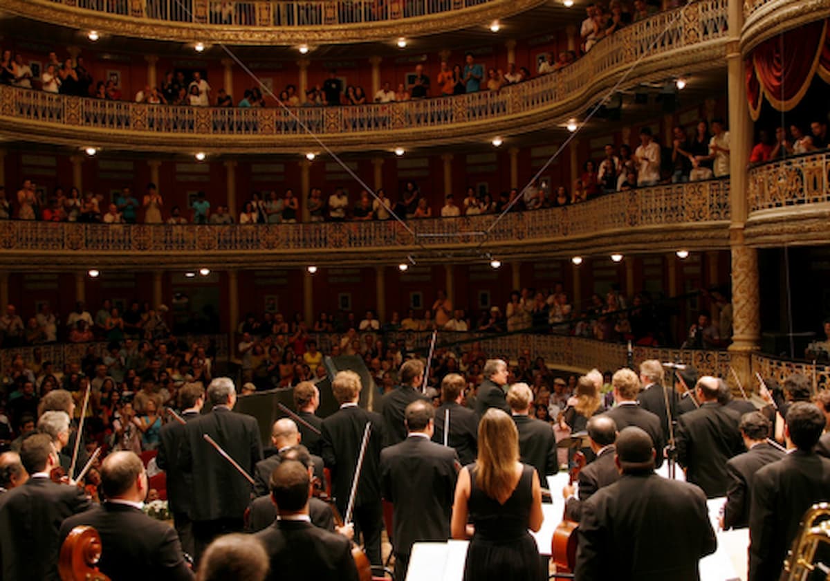 Músicos de orquestra, vestidos de preto e segurando instrumentos, em uma sala de concertos, durante o festival de música Virtuosi Fafael Garcia.