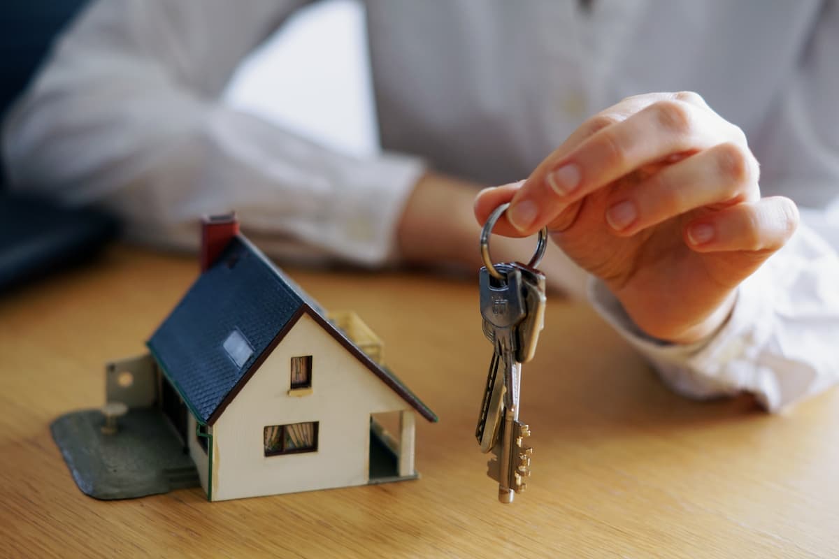Pessoa segurando um molho de chaves apoiada numa mesa com uma casa em miniatura.