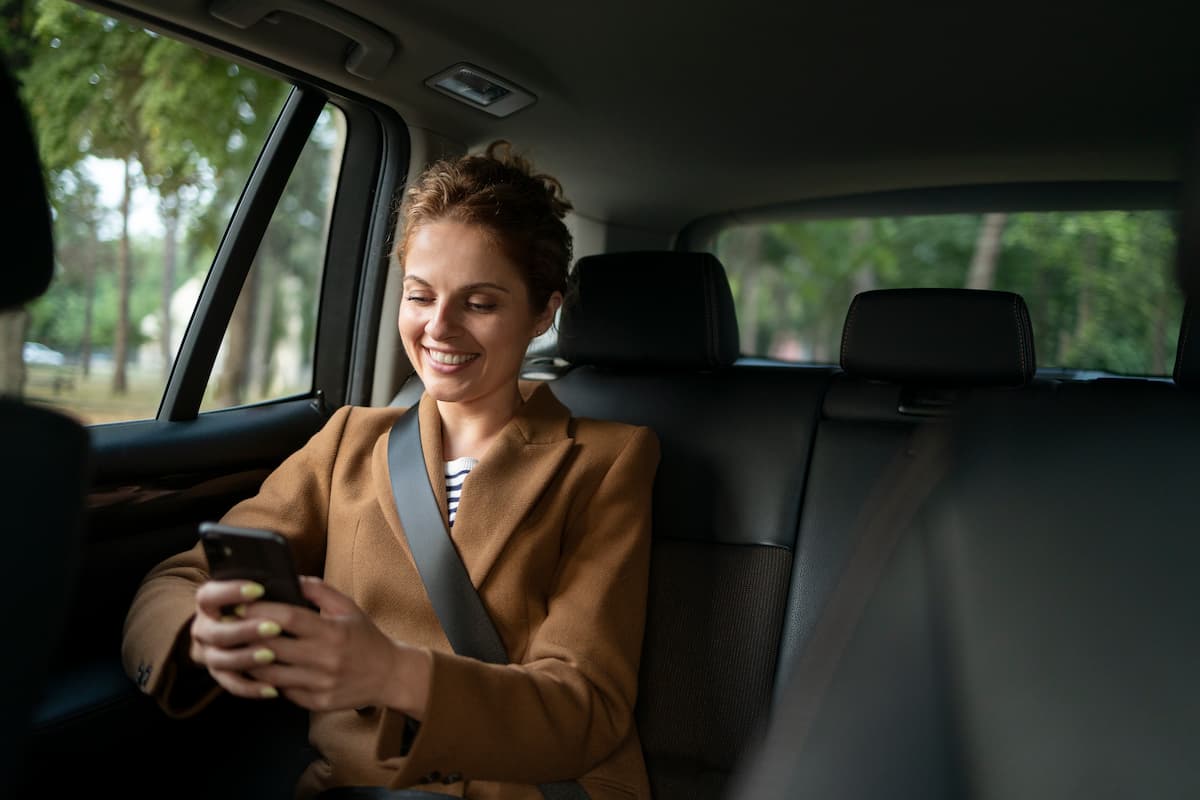 Mulher sorrindo para o celular enquanto viaja no banco traseiro de um uber.