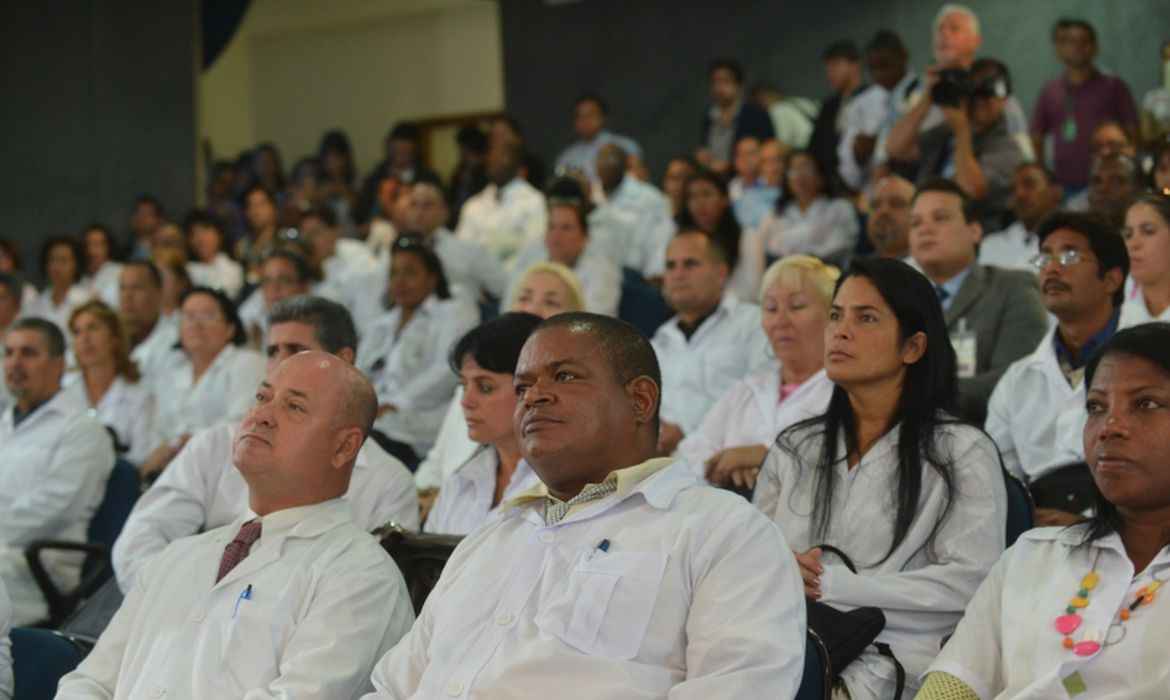 Médicos vestidos com jaleco em um auditório durante reunião do programa do governo.