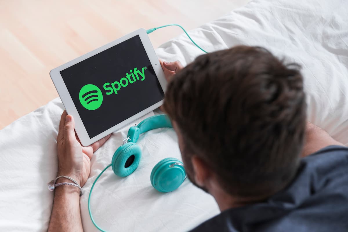 Homem segurando um tablet com a logo do Spotify e um fone de ouvido conectado ao aparelho.