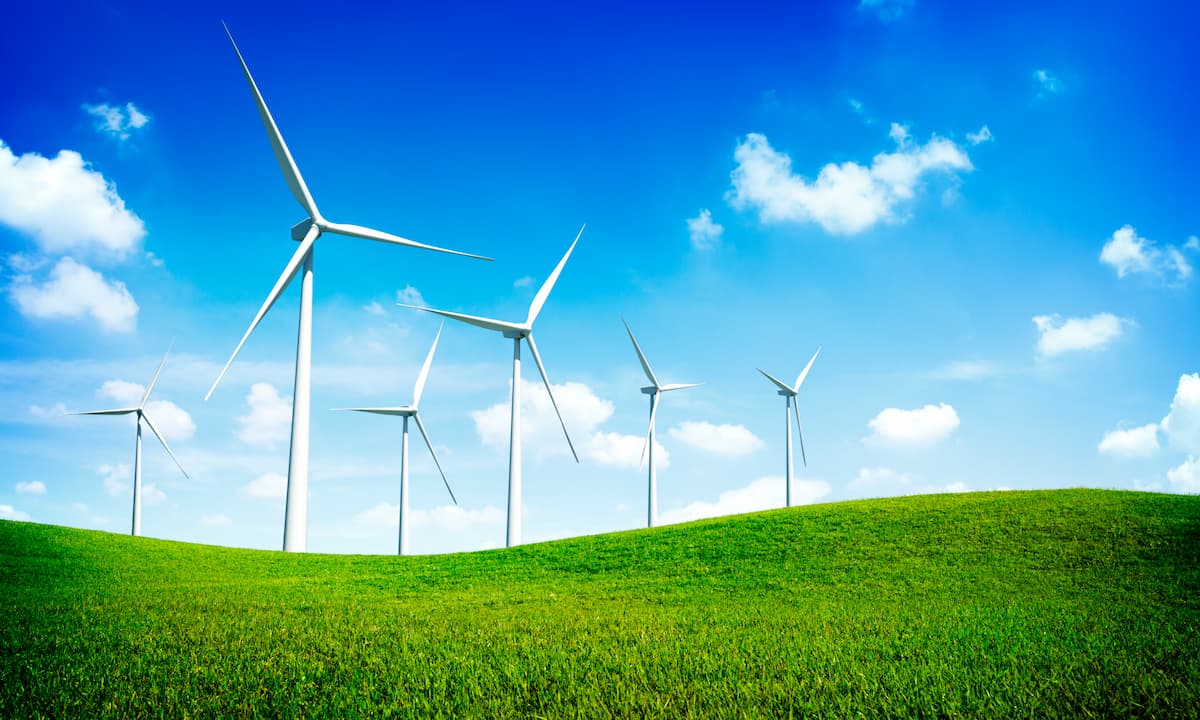 Várias turbinas de energia eólica em um gramado com céu azul.