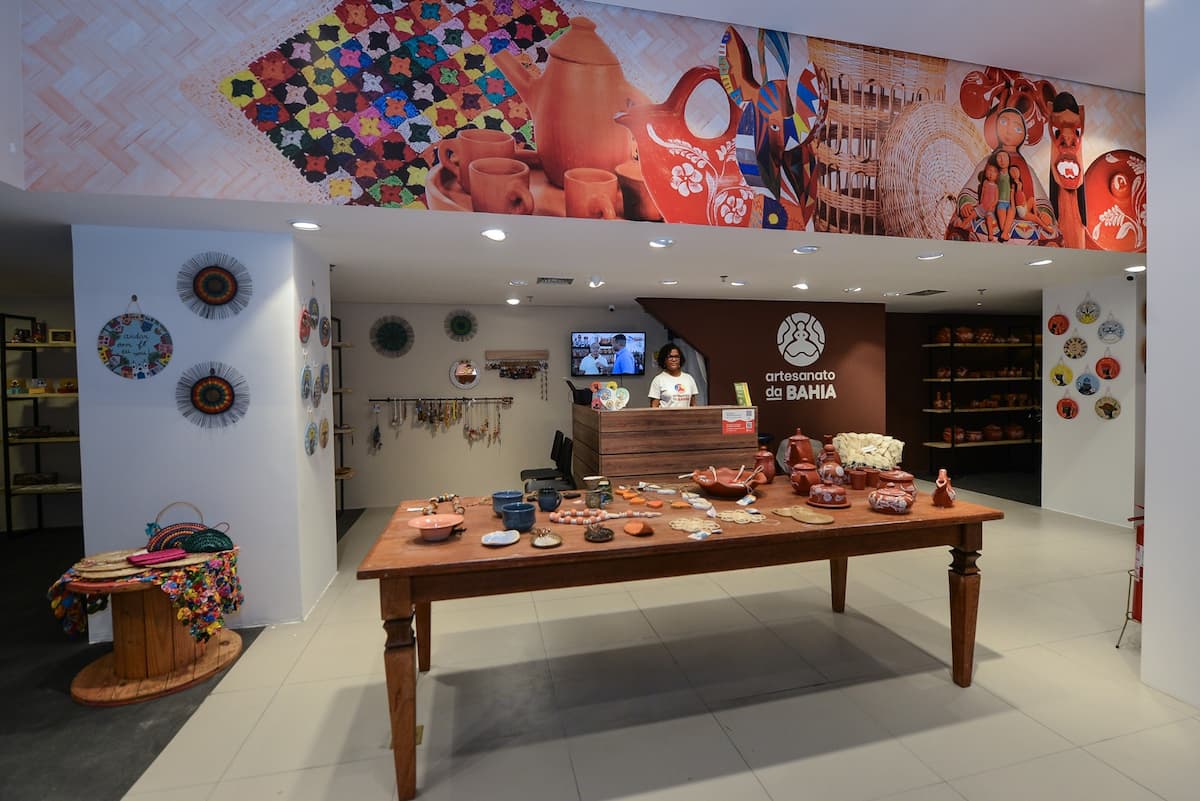 Fachada da nova loja de artesanato no Shopping da Bahia com decoração e materiais expostos e uma funcionária no caixa da loja que predomina nas cores marrom