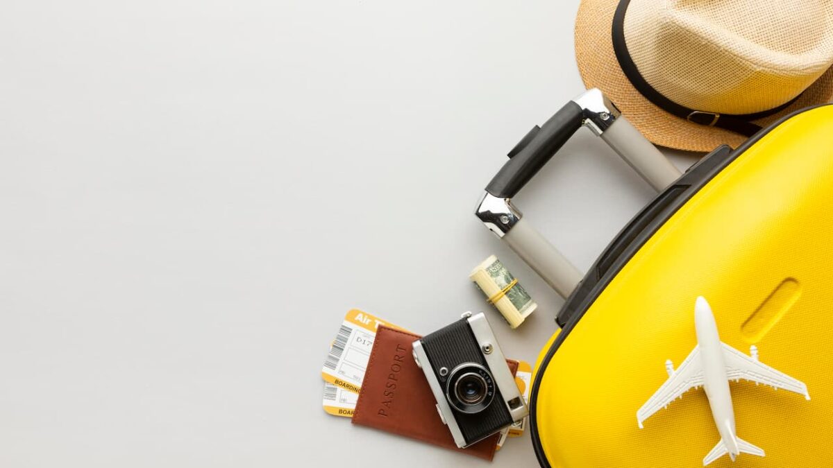 Itens de viagem, como uma mala amarela, um chapéu e uma câmera fotográfica, estão dispostos sobre uma superfície.