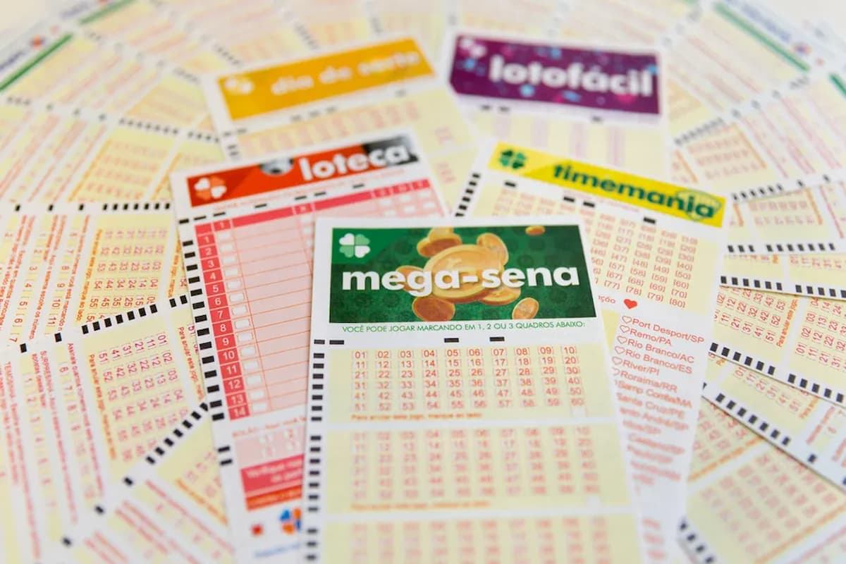 Diferentes cartelas de apostas de loteria, como Mega-Sena e Lotofácil, espalhadas sobre uma mesa.