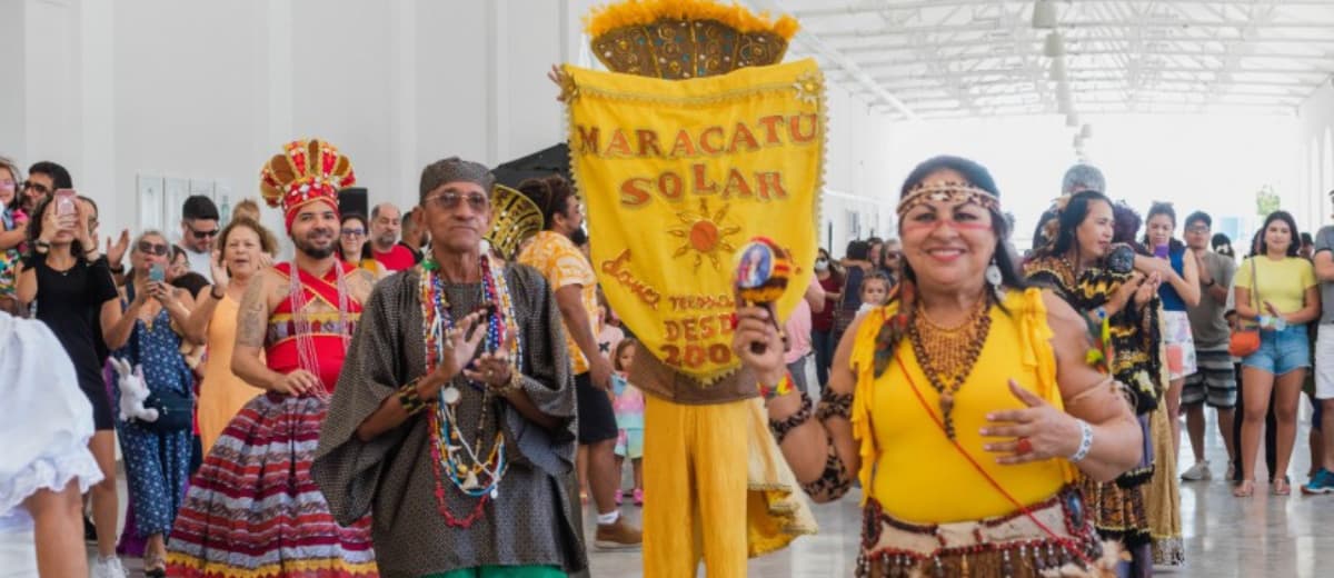Grupo Maracatu Solar durante apresentação. Há diversos membros do grupo com roupas tradicionais e sorrindo, além de uma bandeira com o nome Maracatu Solar e alguns símbolos.