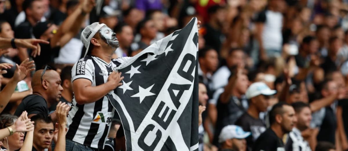 Torcedores do Ceará em estádio, usando uniforme e segurando a bandeira do time.