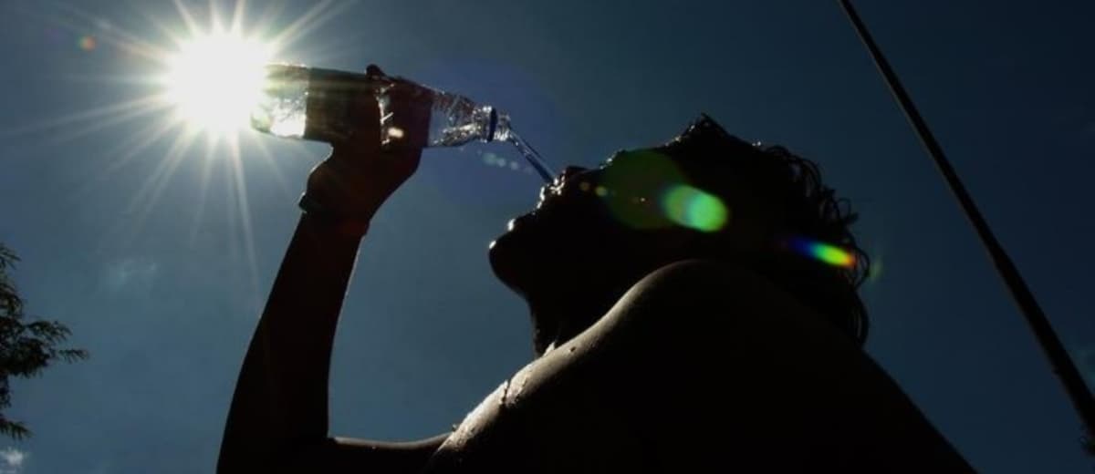 ângulo inferior de homem contra a luz do Sol bebendo água a partir de uma garrafa PET.