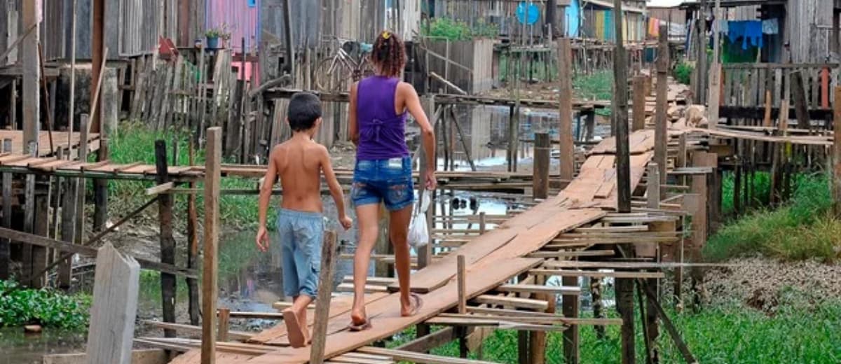 Mãe e filho atravessando ponte suspensa de madeira no Pará.