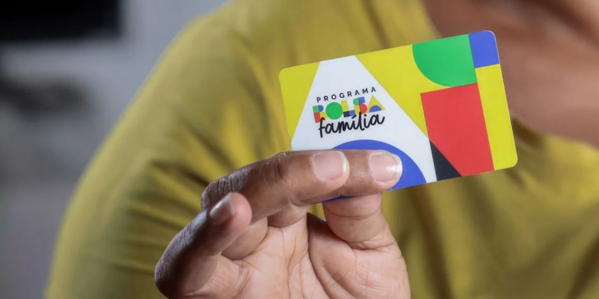 Close up em mão direita de mulher segurando um cartão do Bolsa Família.